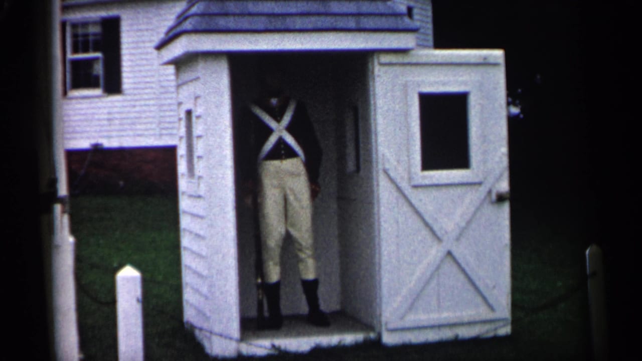 Uniformed person standing inside a small white shed with an open cross-braced door.