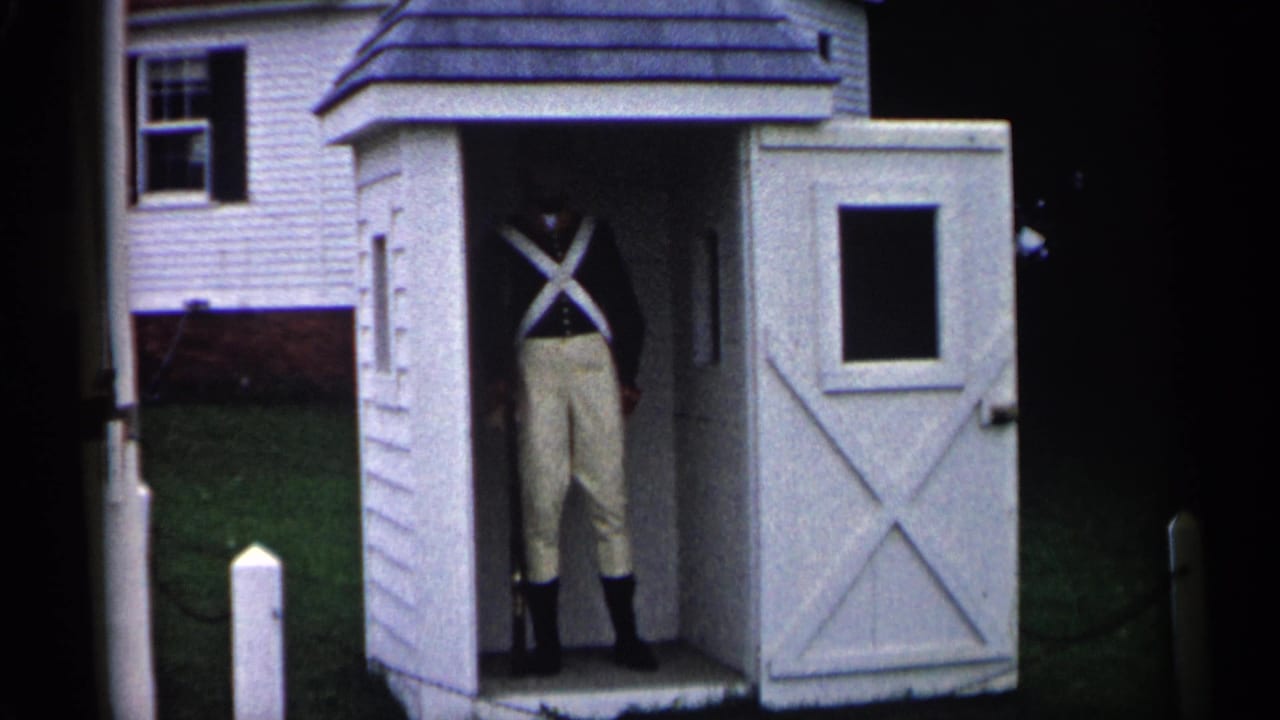 Uniformed person remains inside the white shed with the open door and house behind.