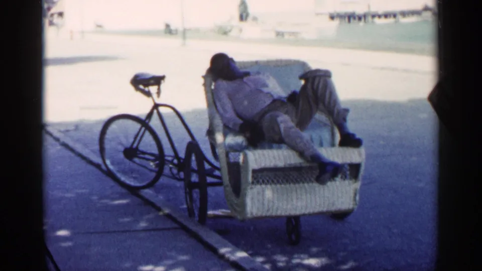 A closer repeated view shows the man asleep or resting in the bicycle passenger cart, with the attached bicycle visible beside him.