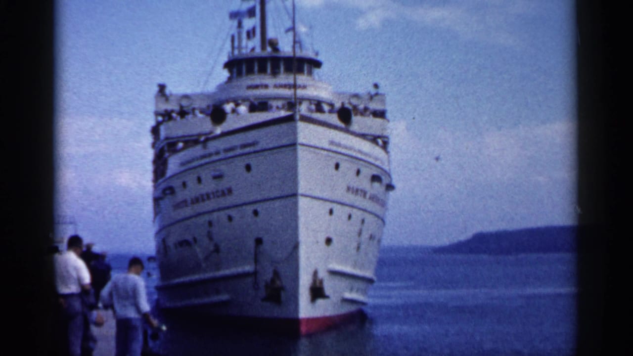 White passenger steamer approaches a dock with people standing at the left edge.