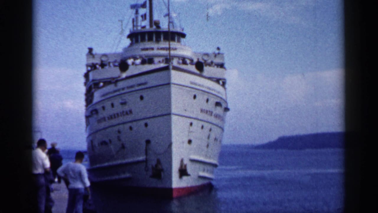 The SS North American nears the Michigan dock, its bow and upper decks visible with people waiting at left.