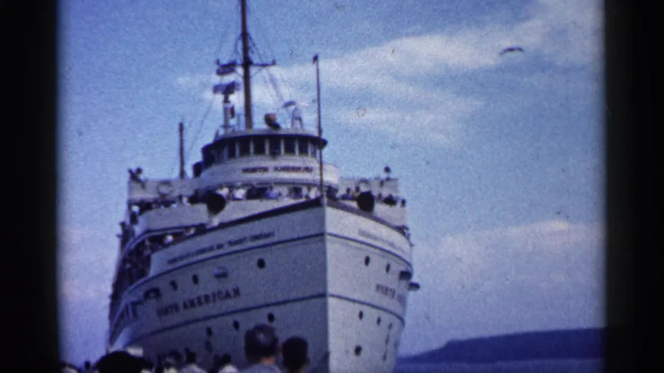 Close 8mm view of the SS North American bow and pilothouse as it approaches port in Michigan, with spectators in the foreground.