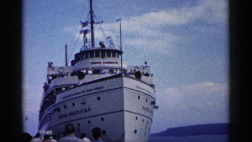 The SS North American remains centered as it comes into port, with dockside figures, open water, and shoreline in view.