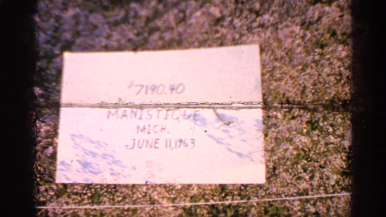 Handwritten paper label on grass reading Manistique, Mich. and June 11, 1960.