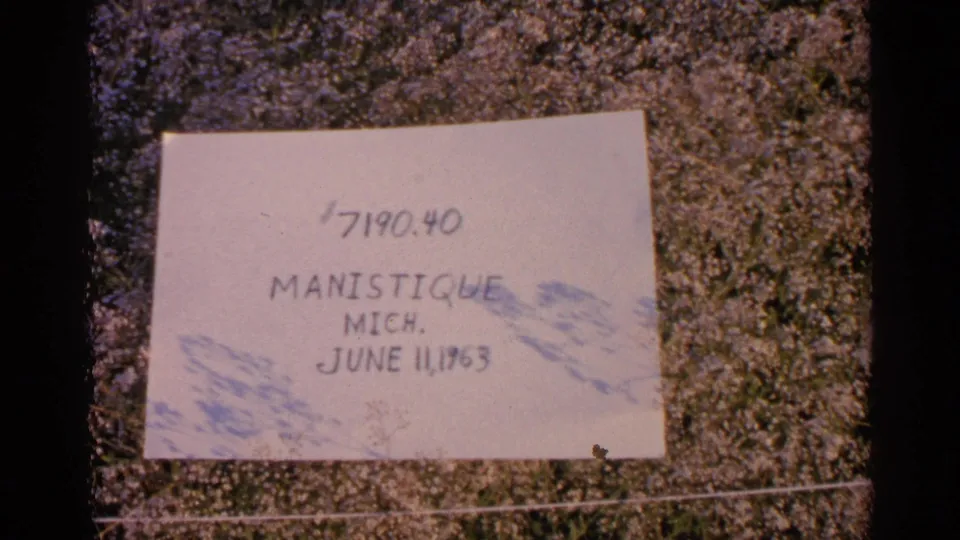 Sunlit handwritten label on grass gives the clip's Manistique, Michigan location and June 11, 1960 date.