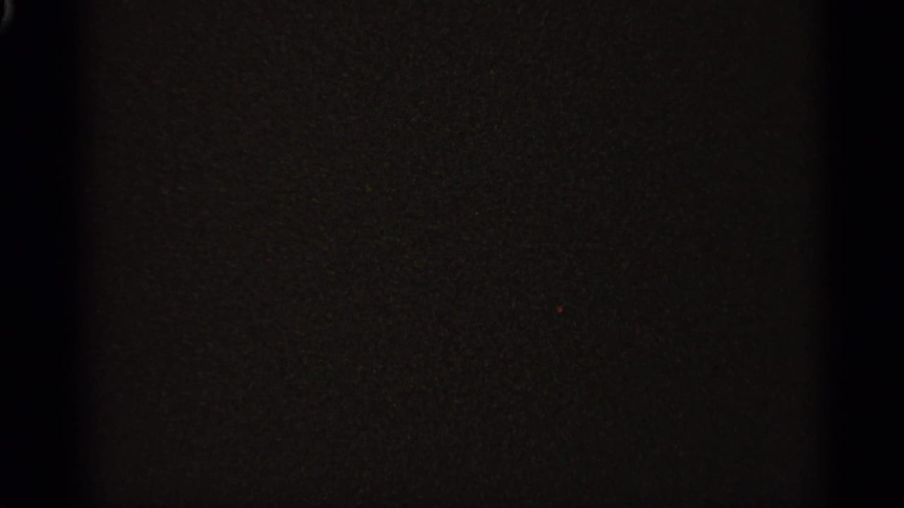 Mostly dark film frame with faint grain and little visible detail.