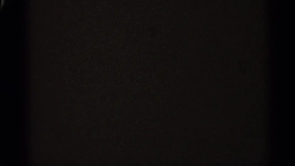 A dark, grainy 8mm frame with minimal visible detail and a faint vertical edge near the left side of the contact sheet.