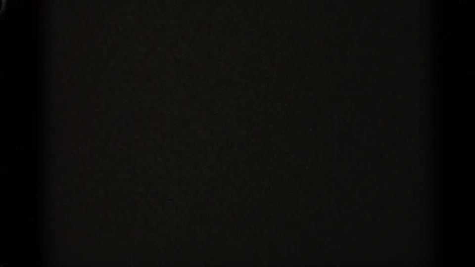 Dark opening frame from an 8mm home movie, with little visible detail beyond film grain and a vertical shadow.