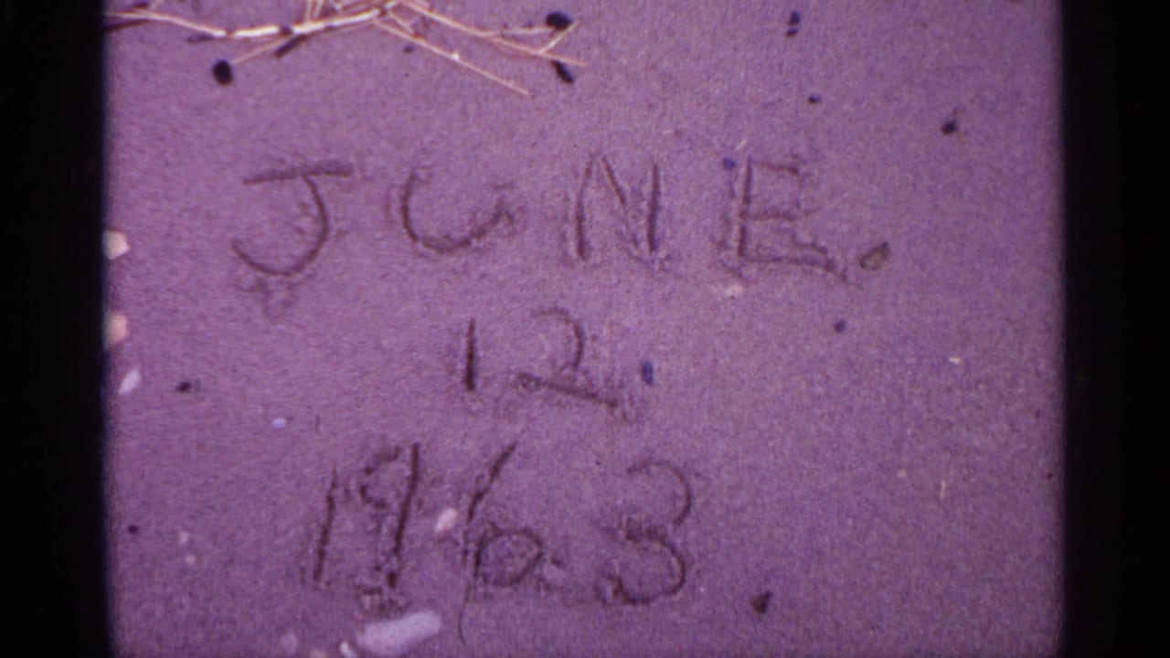 Handwritten date scratched into sand with small twigs near the top edge.