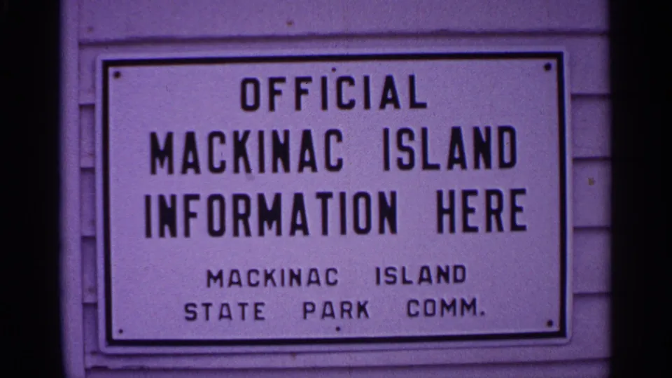 Close 8mm view of a Mackinac Island information sign with bold black lettering and visible purple film cast.