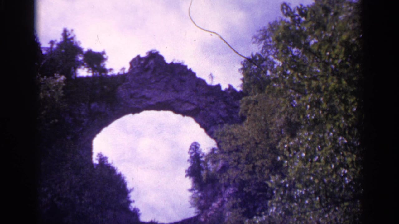 Rocky arch or bridge-like formation partly framed by trees and sky.
