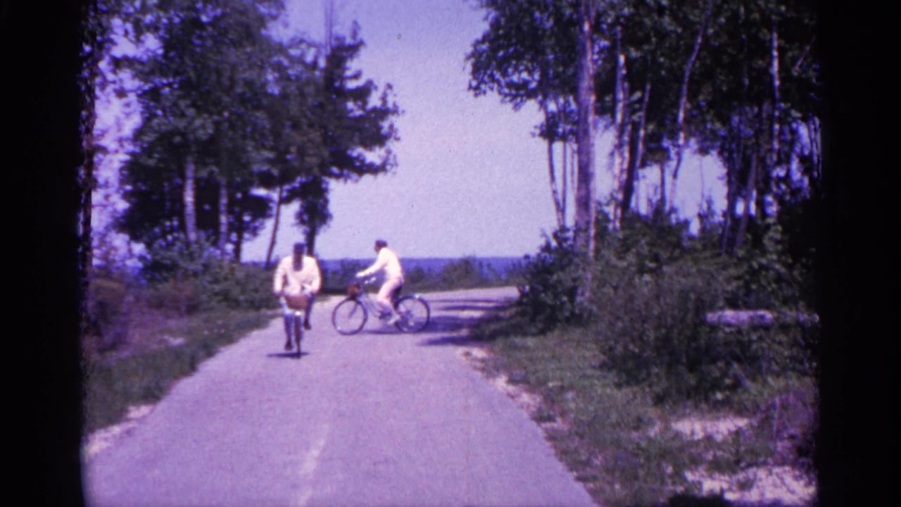 Two adults on bicycles on a paved wooded path with blue water in the distance.