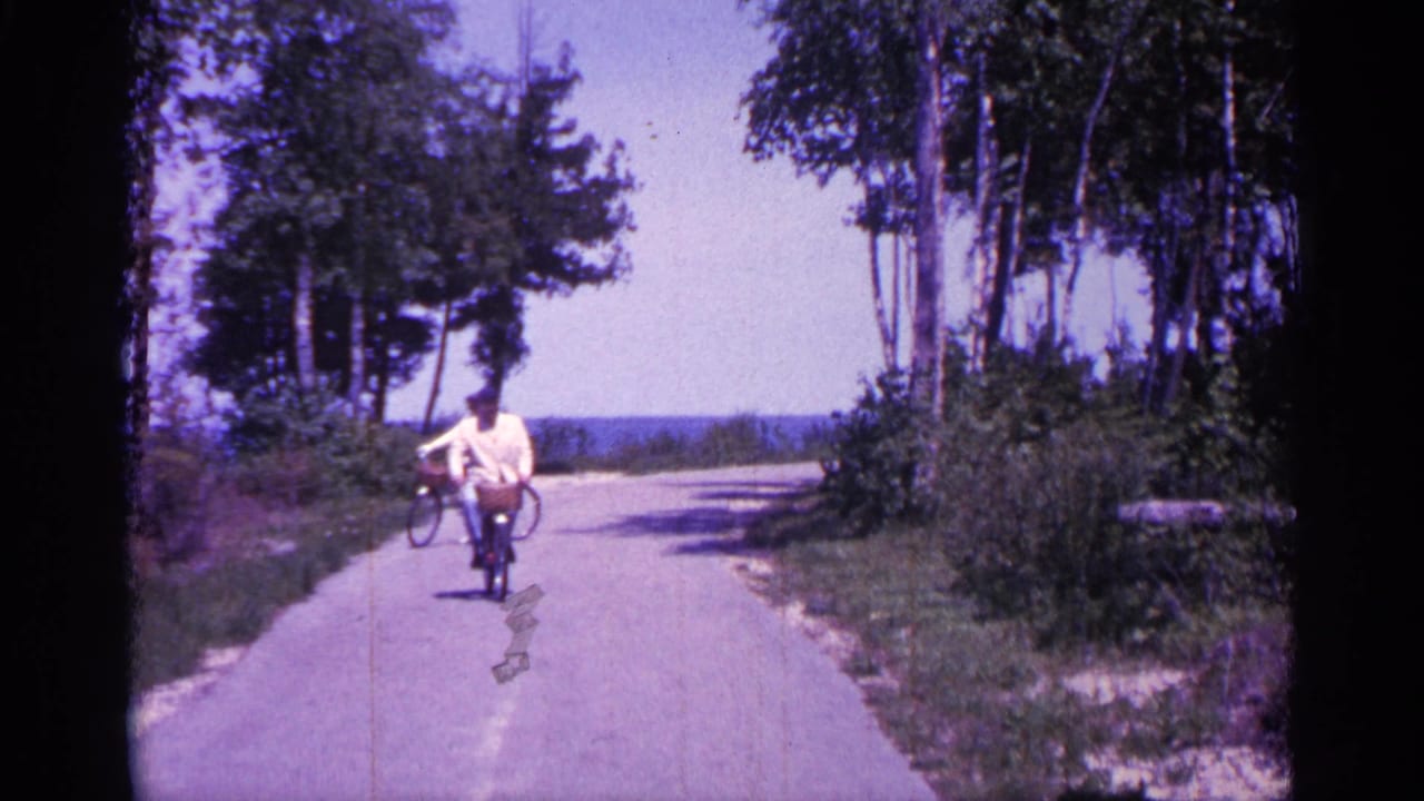 Adult cyclist approaches the camera while another cyclist turns behind on the path.