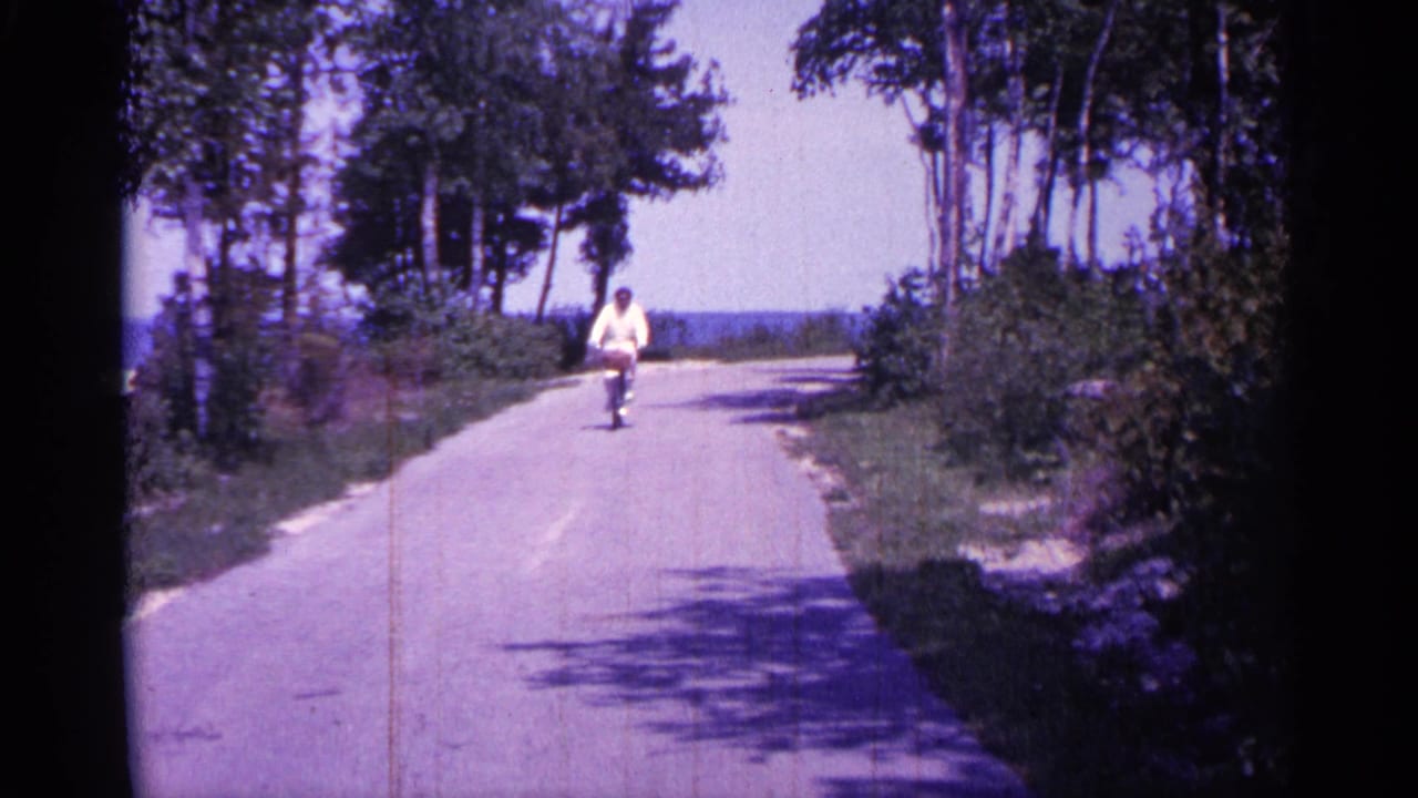 Cyclist in a light shirt rides closer along the empty paved road.