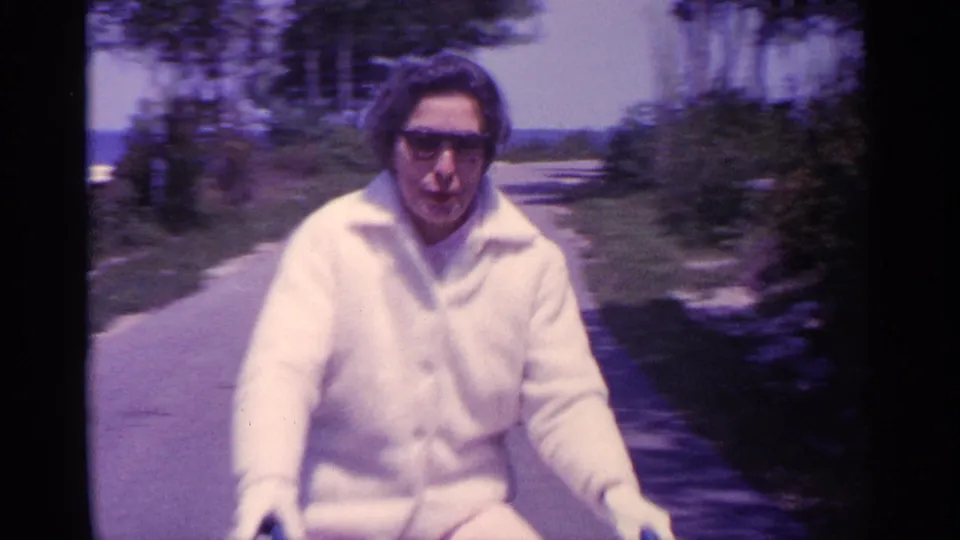 The rider fills the frame as she passes close to the camera, with soft 8mm blur and the path receding behind her.