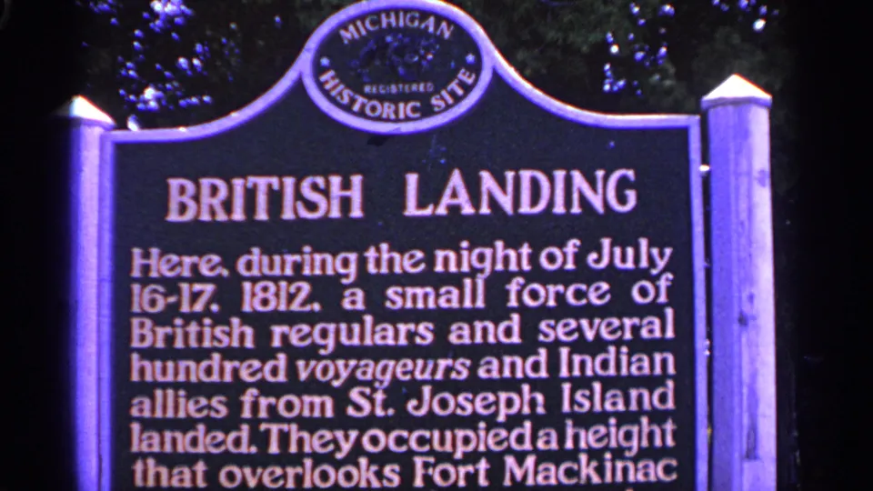 Centered 1960 Michigan home-movie view of the British Landing marker, framed by posts and trees.