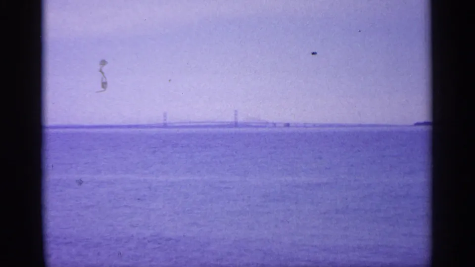 Purple-tinted 8mm view across a Michigan lake toward a distant bridge or causeway under a hazy sky.