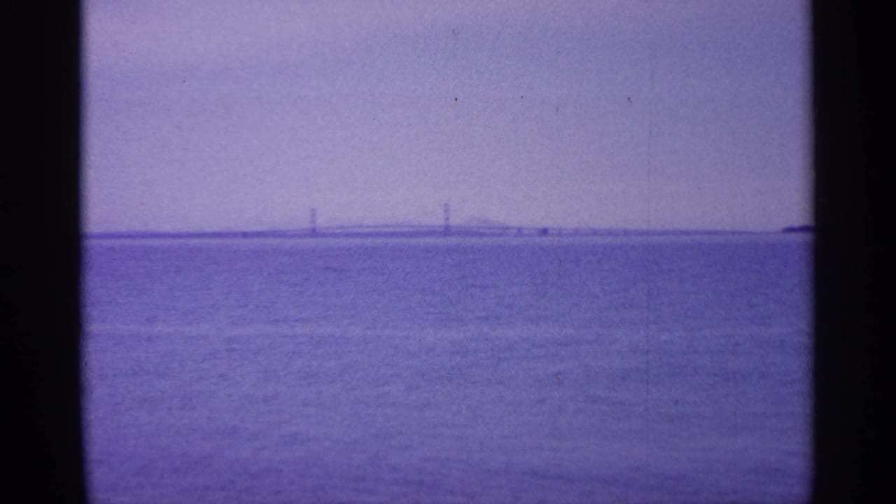 Open water beneath a hazy sky with a distant bridge on the horizon.