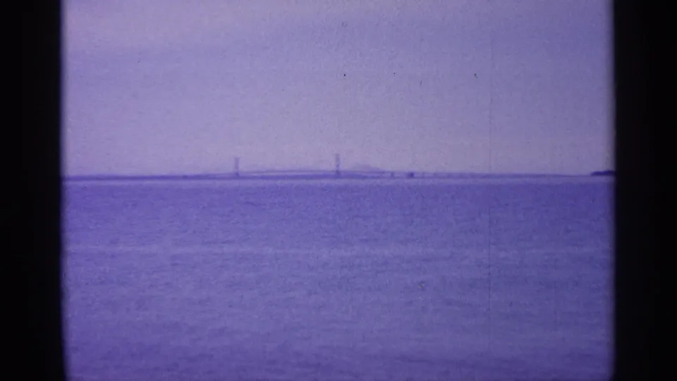 1960 Michigan 8mm frame showing open water, purple haze, and a distant bridge crossing the horizon.
