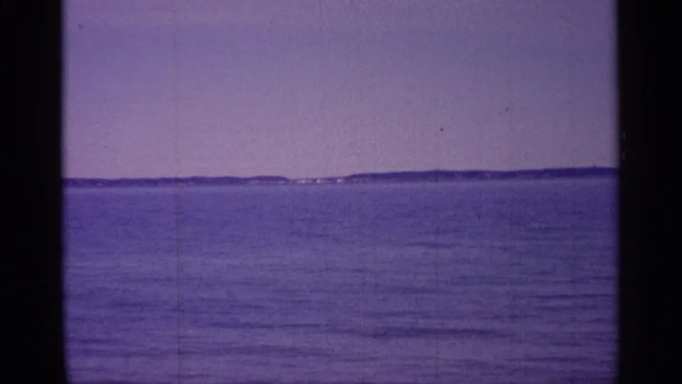 1960 Michigan 8mm frame showing rippled lake water and a low, distant shoreline with faint structures.