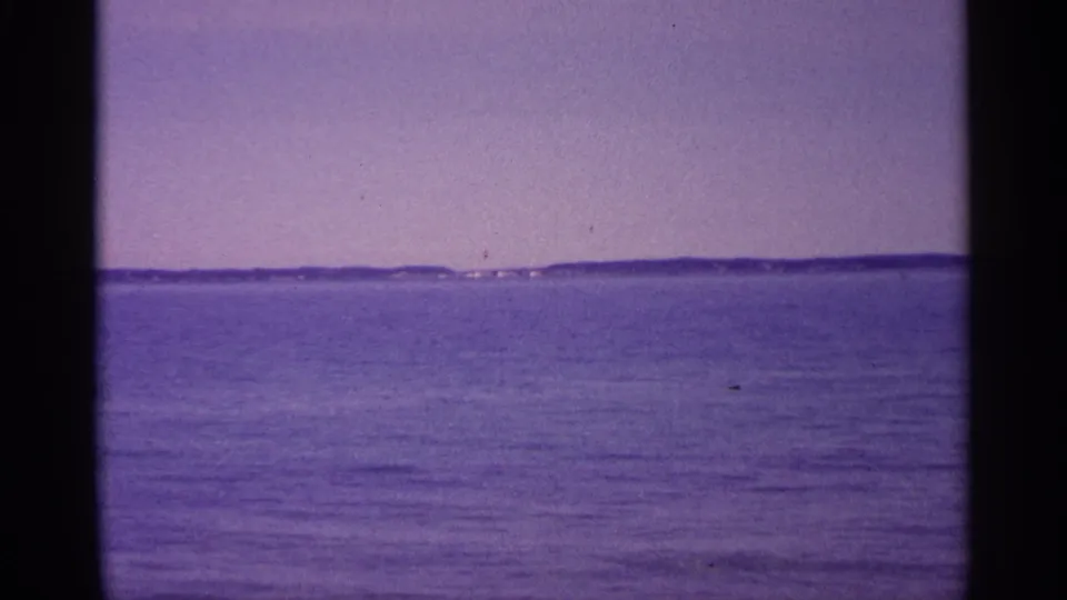 1960 Michigan 8mm frame showing rippled open water and a low island or shoreline on the horizon with visible film borders.