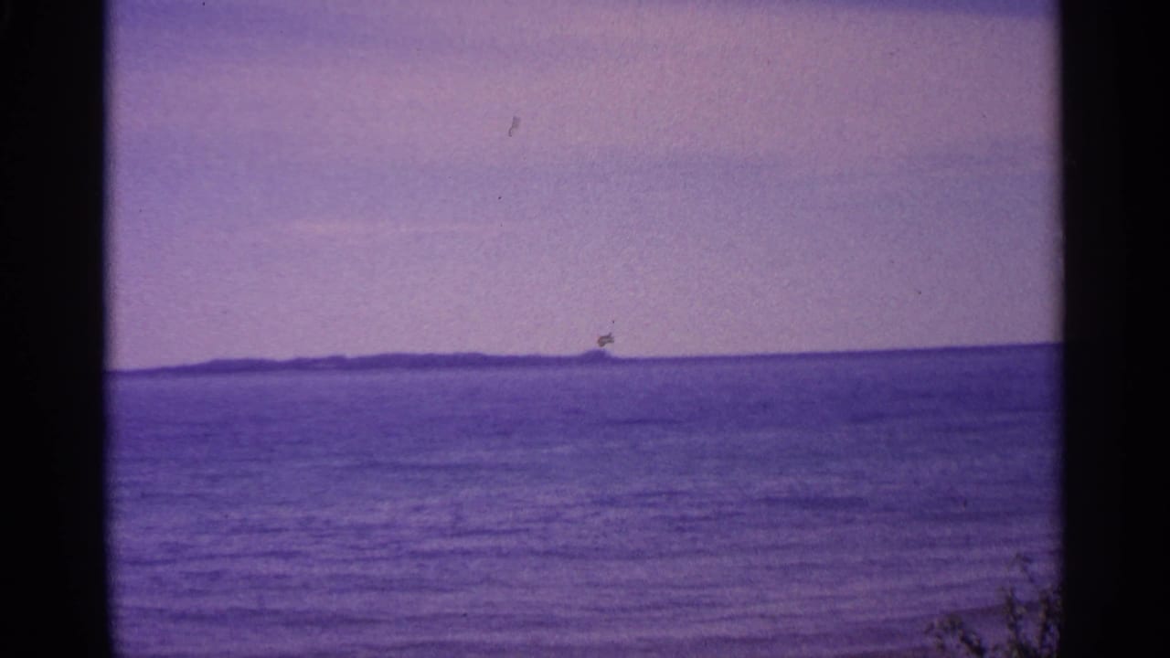 Wide water horizon with a distant low island and dark film borders.