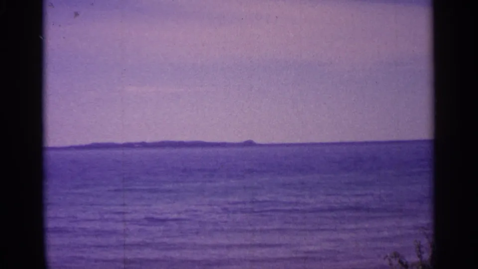 1960 Michigan 8mm frame of a calm broad water surface, low horizon, and distant dark shoreline or island.