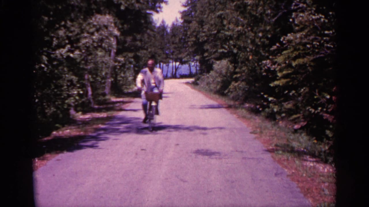 The rider appears farther along the shaded Michigan road, pedaling toward the camera through bright summer greenery.