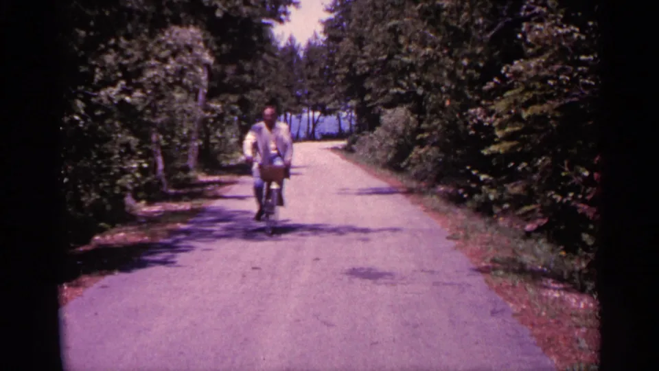 The rider appears farther along the shaded Michigan road, pedaling toward the camera through bright summer greenery.