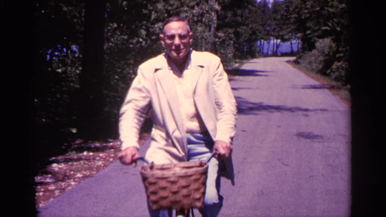 Smiling man on a bicycle nears the camera with a wicker basket on the handlebars.