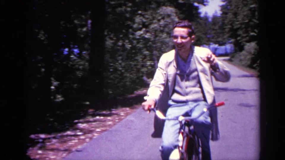 The bicyclist smiles and raises a hand in greeting as he passes close to the stationary camera on the Michigan road.