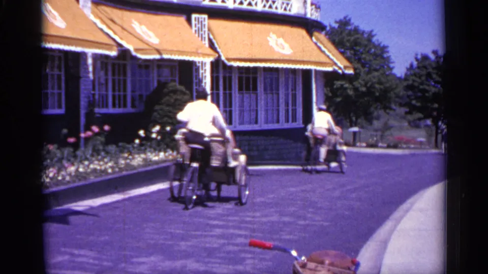 The final frame shows rickshaw-style carts moving away along a curved paved path beside orange awnings, flowers, and trees in Michigan.