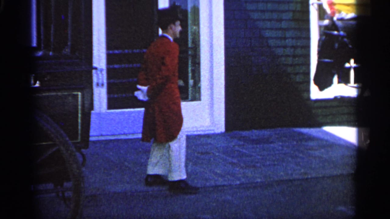 1960 Michigan 8mm frame showing a man in a red coat and top hat beside a building entrance at night.