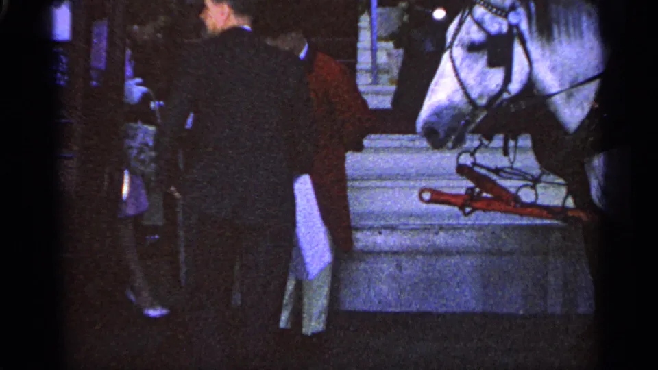1960 Michigan 8mm frame showing the red-coated attendant and suited man near a harnessed white horse by stone steps.