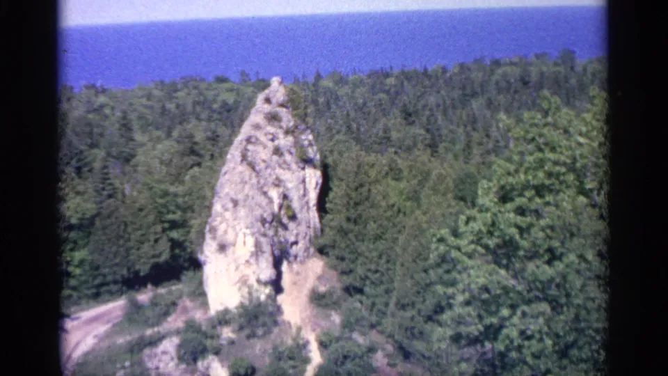 The final 8mm frame holds on the forested Michigan overlook, centered on a pale rock outcrop and distant blue water.