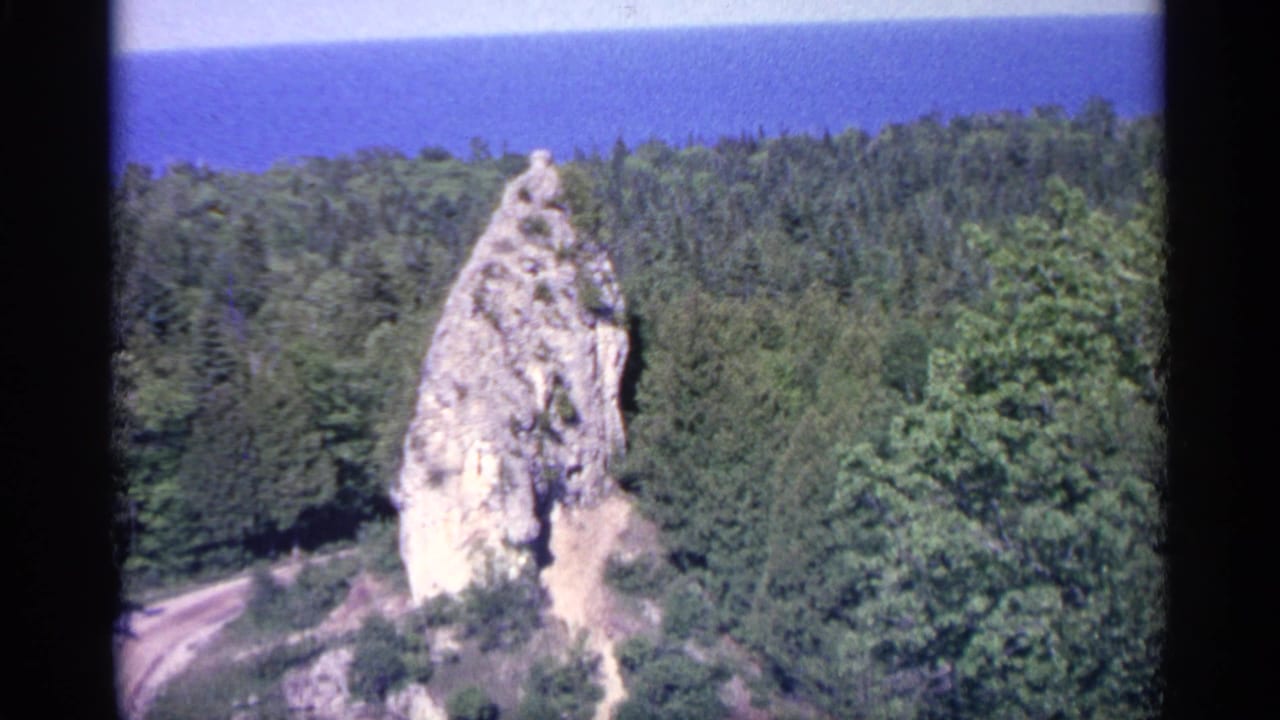 Tall rock formation above dense forest with blue lake horizon in the distance.
