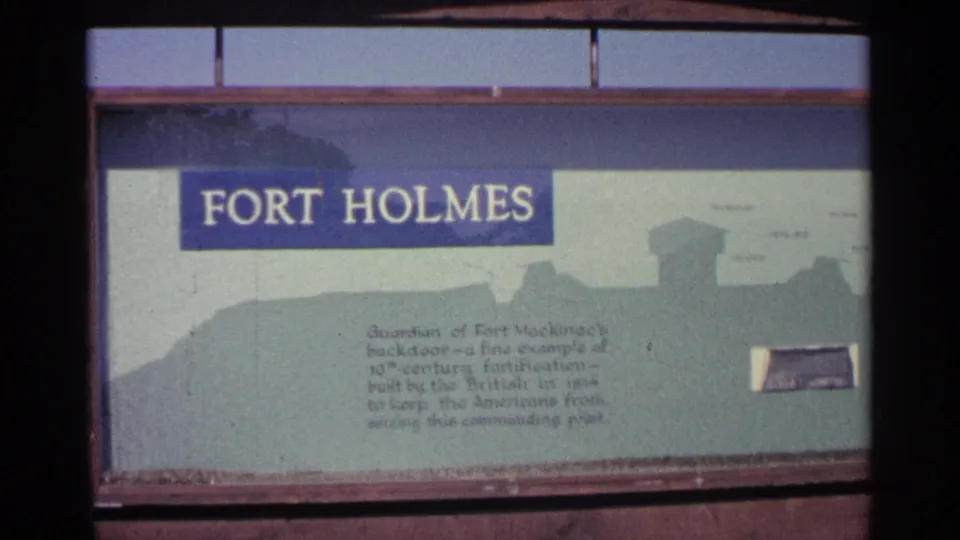 1960 Michigan footage frames the Fort Holmes sign closely, showing the title, printed historical text, and a pale silhouette of fort structures.