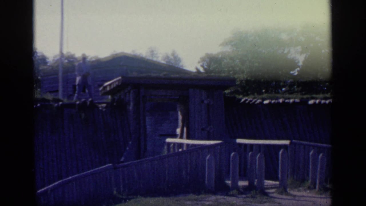 Wooden fort fence and ramp leading toward a timber structure under bright sky.