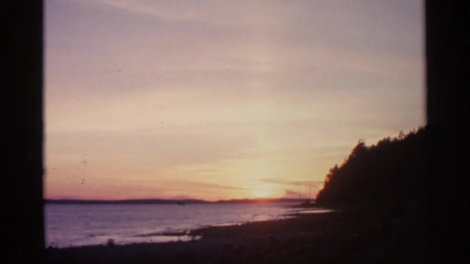 1960 Michigan 8mm frame showing a lakeside or waterside sunset with silhouetted trees and a glowing horizon.