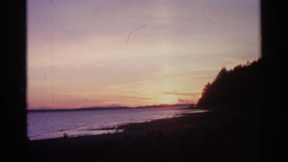 1960 Michigan 8mm frame with pastel dusk light, open water, distant shore, and a shadowed wooded bluff.