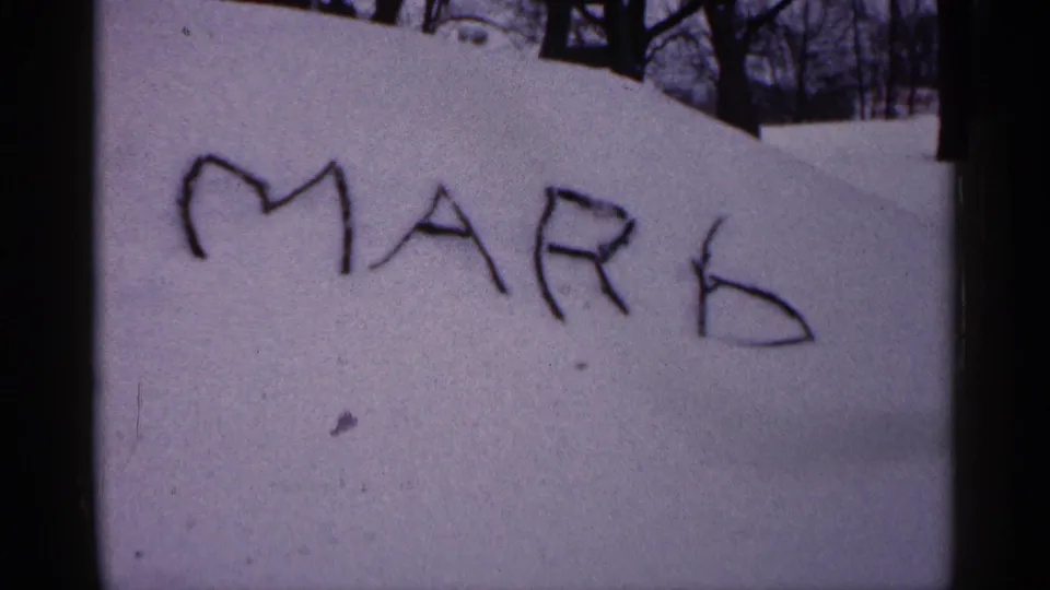 A closer 8mm frame shows MARK traced into the snow, likely part of the same Minnesota winter yard scene.