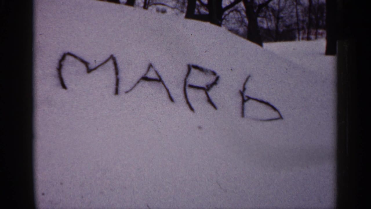 1961 Minnesota 8mm frame showing MARK written in snow on a buried car, with bare trees and a snowy yard behind it.