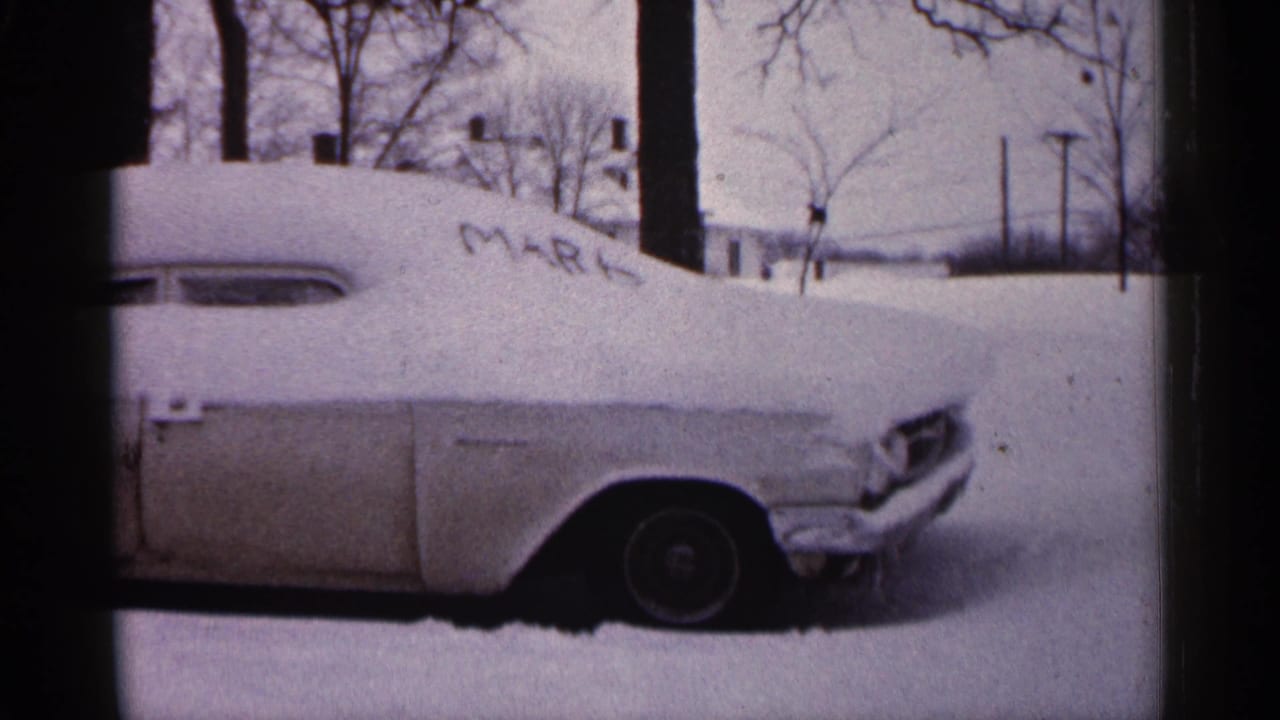 1961 Minnesota frame of a mid-century car nearly covered by snow, with MARK visible on the hood area and winter trees behind.