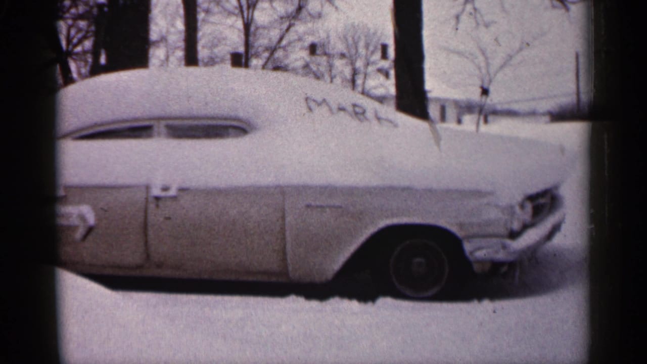 1961 Minnesota 8mm frame showing a snow-covered vintage car with bare trees and a house in the background.