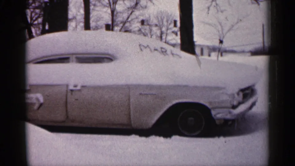 1961 Minnesota 8mm frame showing a snow-covered vintage car with bare trees and a house in the background.