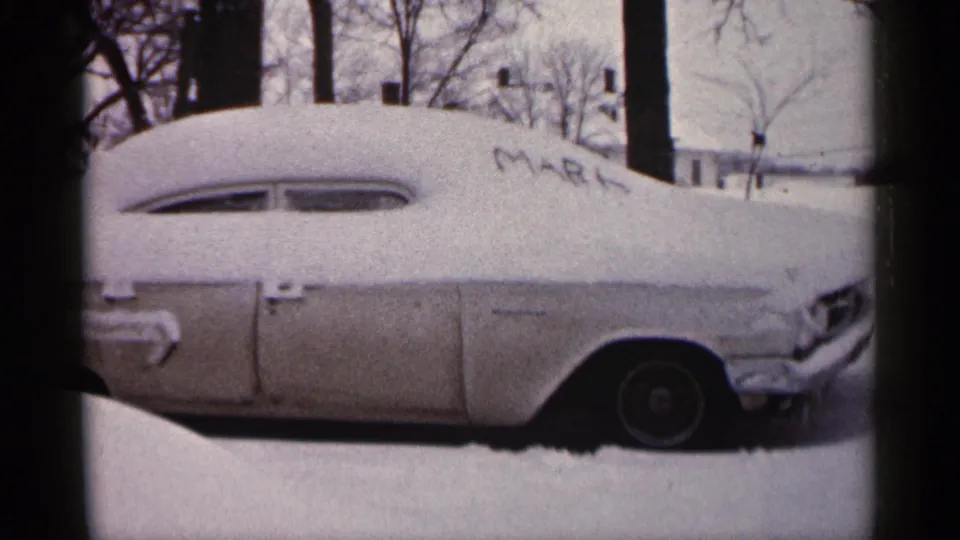 1961 Minnesota frame showing the side of a snow-covered vintage car, with MARK traced into the roof snow.