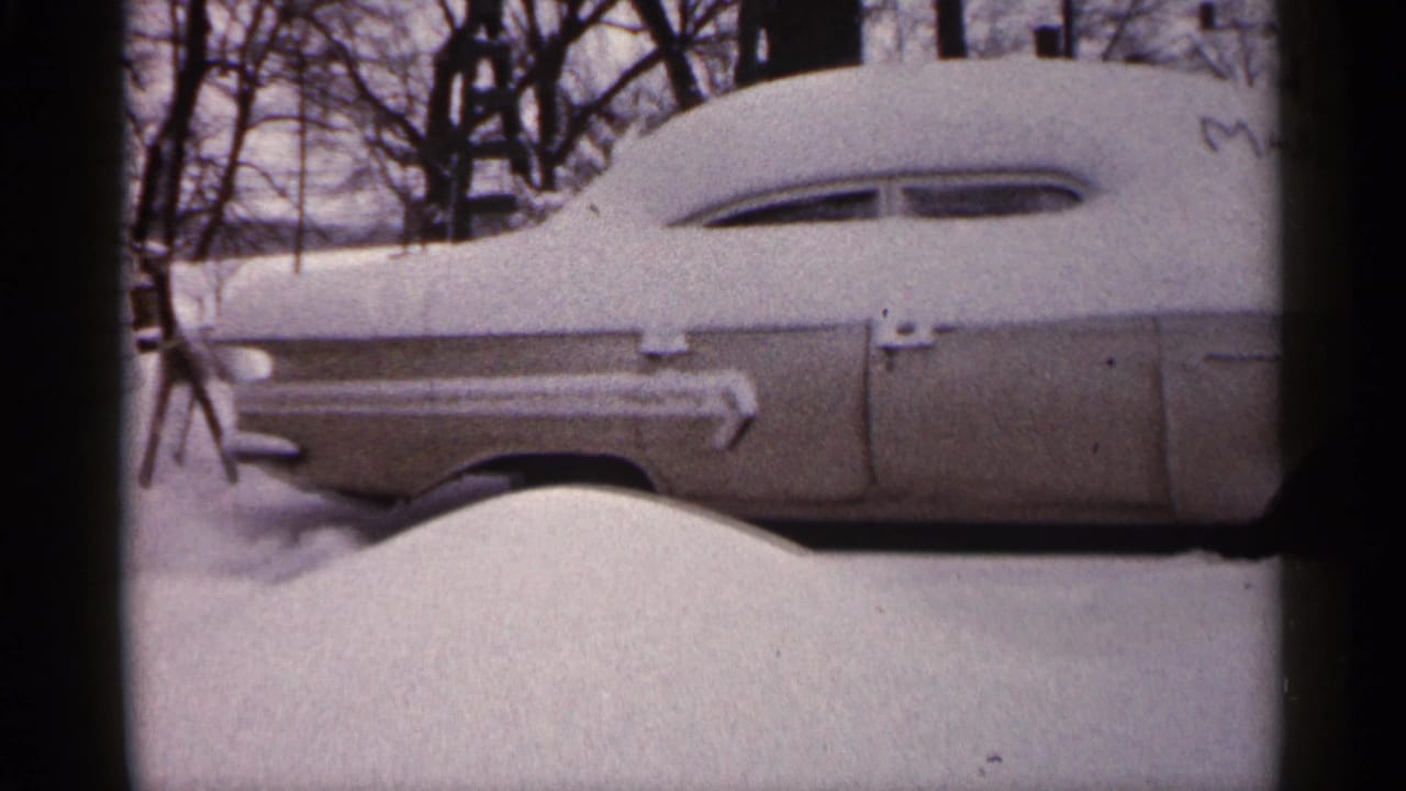 Older car covered with snow, seen from the side in a winter yard.