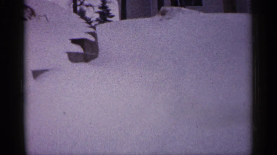 1961 Minnesota 8mm frame showing a snow-blanketed residential yard, a low object partly buried in snow, and partial house detail near the top.