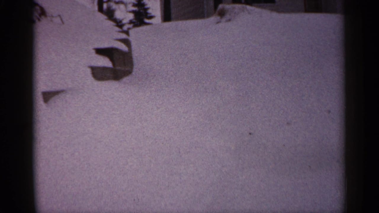 1961 Minnesota 8mm frame showing deep snow against a residential exterior, with a window area and dark branches above.