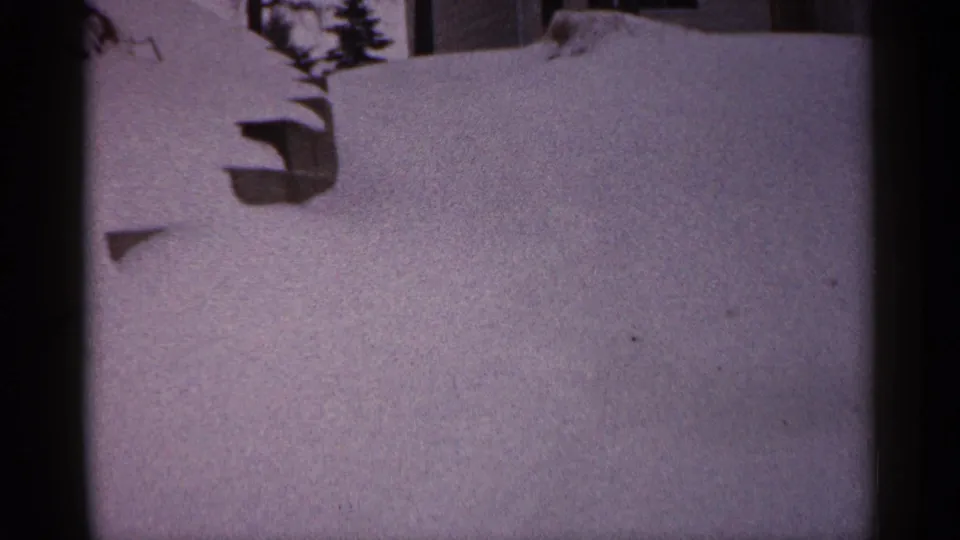 1961 Minnesota 8mm frame showing deep snow against a residential exterior, with a window area and dark branches above.